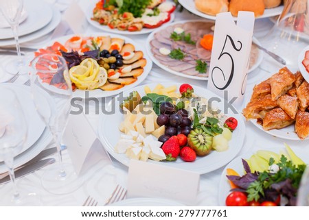 Buffet table served with tasty meals. Cheese platter garnished with fresh strawberries, kiwi, grapes and mint