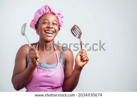 cheerful african lady holding kitchen wares, black girl in apron and a head wrap excited- indoor food concept