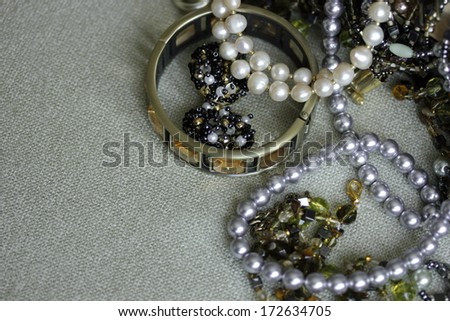 art gold, black and white bijouterie with white and light lilac pearl on light textile background in sepia