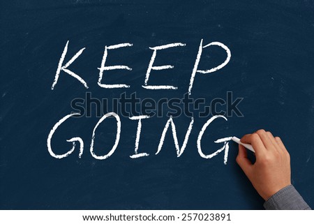 Keep Going on blue chalkboard with the hand of businessman.