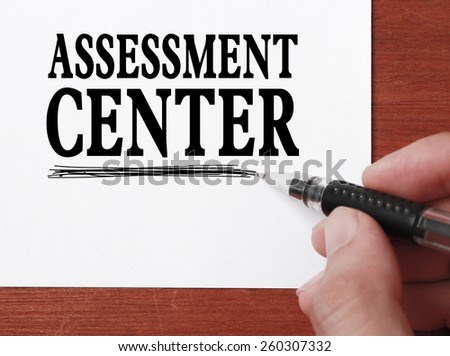 Businessman is writing Assessment center text on white paper.