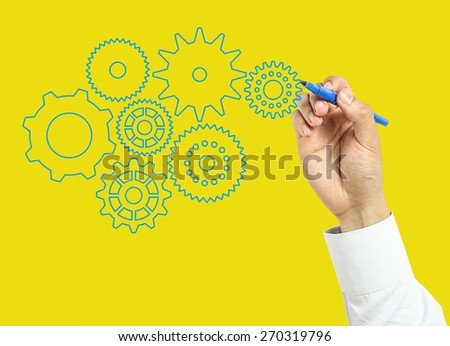 Businessman is drawing gears with marker on transparent board with yellow background.