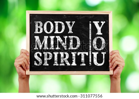 Hands holding blackboard with text Body Mind Spirit You against green blurred background.