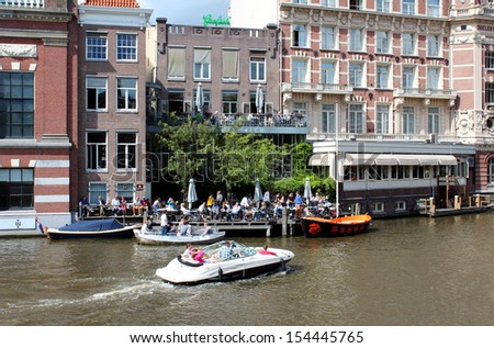 Amsterdam, Netherlands- August 10, 2013: Tourists enjoying a boat ride whilst local residents eat in the restaurant on the canal side.