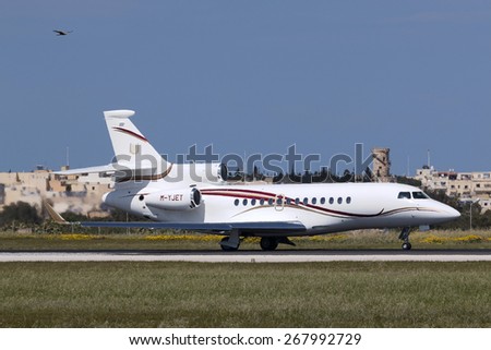 Luqa, Malta April 9, 2015: A private Dassault Falcon 7X backtracks runway 31, while a real Falcon (actually I think it\'s some type of harrier) flies alongside. A \