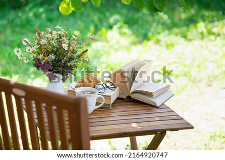 Bouquet of meadow flowers, croissant, cup of tea or coffee, books on table in summer garden. Rest in garden, reading books, breakfast, vacations in nature concept. Summertime in garden on backyard Сток-фото © 