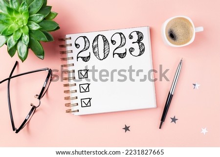 New year resolutions 2023 on desk. 2023 resolutions list with notebook, coffee cup on pink background. Goals, resolutions, plan, action, checklist concept. New Year 2023 template, copy space Foto d'archivio © 