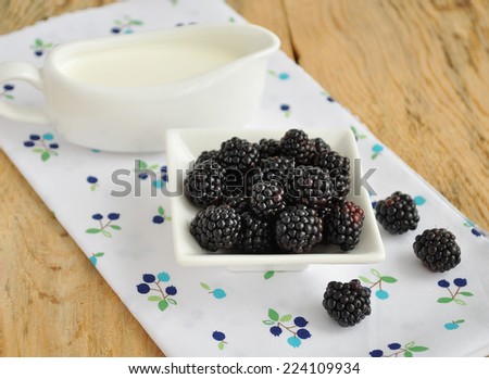 Blackberries in a bowl and cream on textile napkin