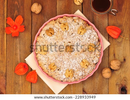 Apple pie with walnuts and powdered sugar in a ceramic lilac form, a cup of coffee and physalis on a brown wooden background. Top view