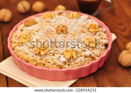 Apple pie with walnuts and powdered sugar in a ceramic lilac form, a cup of coffee on a brown wooden background