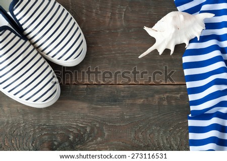 Shoes, sea shell and striped cloth on old wooden background. Top view sea shoes