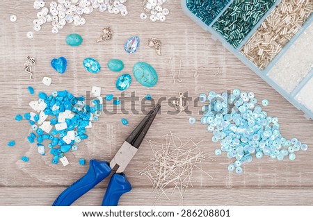 Crystals, pendants, charms, plier, glass hearts, box with beads and accessories to create hand made jewelry on old wooden background. Top view