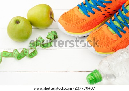 Sport shoes, apple and bottle of water on white wooden background. Sport equipment. Selective focus