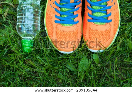 Sports shoes sneakers and bottle of water on a fresh green grass. Sport equipment top view. Sports in the open air.