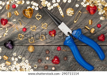 Tools for handmade jewelry. Beads, plier, glass hearts and accessories to create hand made jewelry on old wooden background. Top view