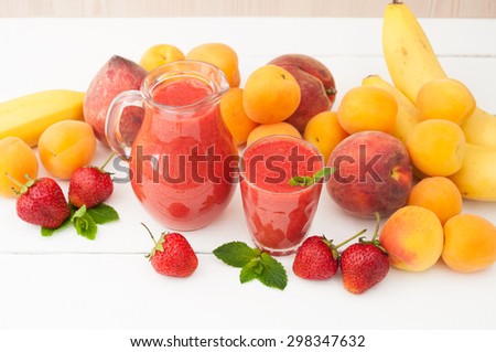 Healthy food. Strawberry banana smoothie with mint in a glass and pitcher on white wooden background. Fresh fruits bananas, peaches and apricots background. Selective focus.
