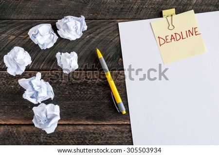 Sticky note with the word Deadline. White blank paper, crumpled paper and pen on a wooden background