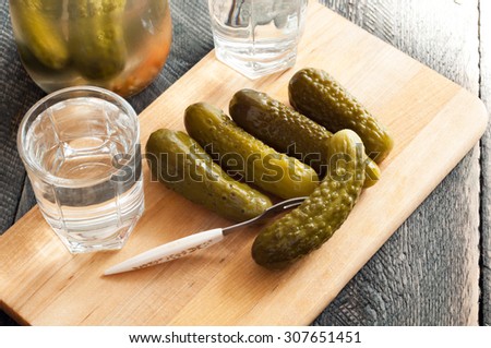 Pickled cucumbers and shot glass of vodka on wooden background. Rustic style