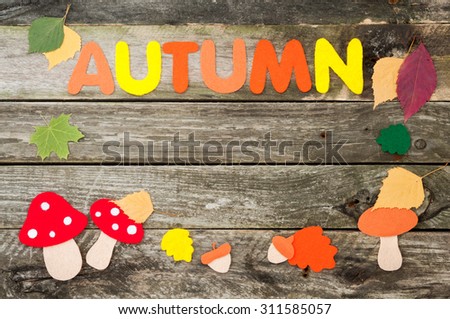 Handmade autumn frame on old wooden background. Handmade leaves, mushrooms, acorns and word Autumn made of felt. Top view