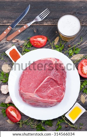 Raw beef with herbs, spices, vegetables and beer in a glass on a wooden background. The ingredients and the cooking process. Rustic style