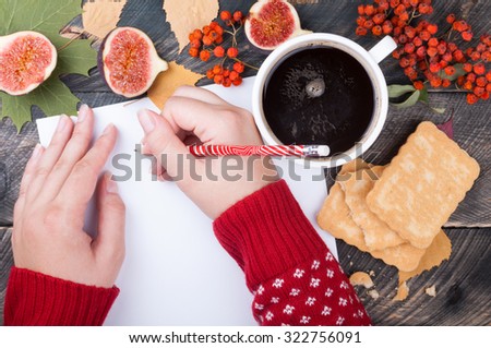 Woman\'s hands writing on a blank sheet of paper on a wooden background. Concept  woman writing a letter or note in a cozy atmosphere with a cup of coffee. Top view