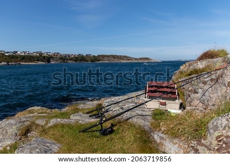 Box with fishing accessories on the cliff of the fjord. Fishing rods lying on the rock. Rocky cliffs by the fjord, a place next to the main road with a beautiful view of the fjord in Norway