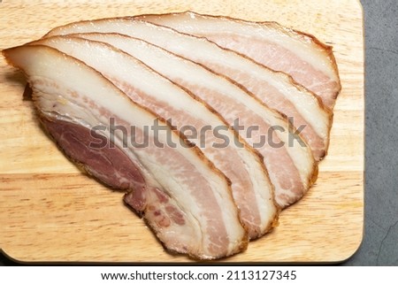 Guanciale dried speck а ham. Italian cured meat product prepared from pork jowl or cheeks sliced on wooden board.  Сток-фото © 