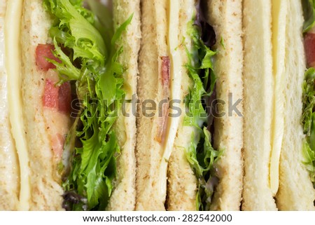 Sandwiches in box for a picnic ; whole wheat bread, baby green and red oak leaf lettuce, bacon, cheese and mayonnaise