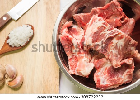 Raw pork ribs in stainless steel bowl and ingredients on a cutting board