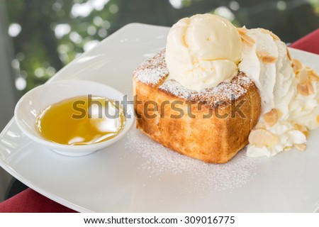A luscious honey toast with vanilla ice cream on top ; whipped cream and almond slice