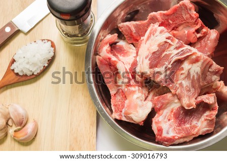 Raw pork ribs in stainless steel bowl with ingredients on a cutting board