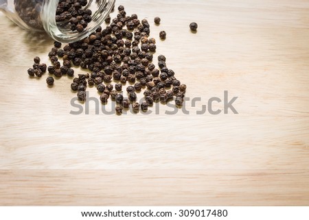 Black pepper spilled out on wooden background with copy space