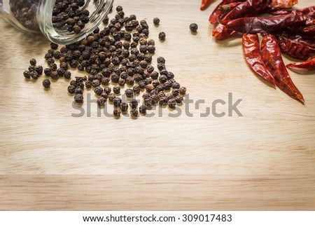 Black pepper spilled out with dried chili on wooden background with copy space