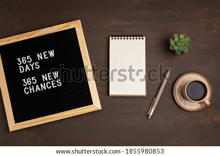 365 new days, 365 new chances. Letter board with motivational quote on dark wooden background with notepad , pen, coffee and succulent. New year’s resolutions mockup. Flatlay, top view