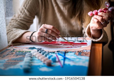 Painting for beginners, a woman draws a picture by numbers with acrylic paints on canvas,painting a picture with a brush, a girl draws a picture, self-isolation, home hobby, creativity at home