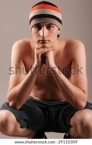 Young man in knitted cap and shorts sitting on grey background