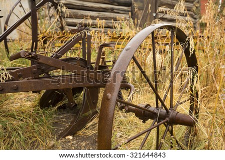 Antique plow with metal wheels, in grass next to front of log cabin, Jackson, Wyoming, on a rainy summer day, close up.