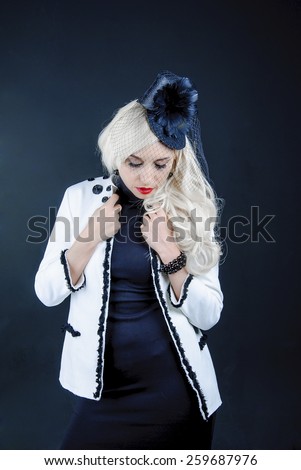 blonde with long hair in a white jacket black dress with a hat with feathers looks down