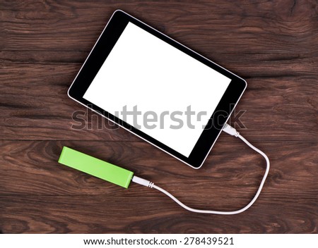 Tablet PC charged by the mobile charger on a wooden brown background