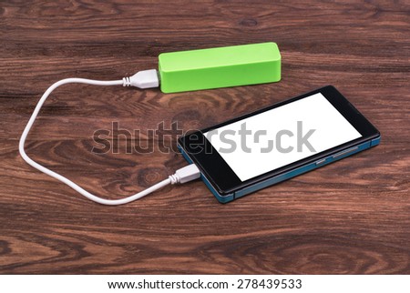 Charging smartphone battery power bank on wooden background