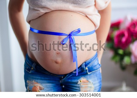 A pregnant woman close up with a blue ribbon tied on the tummy
