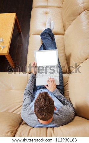 Man stretched out on sofa using a modern laptop - Clipping path for laptop screen