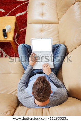 Man sitting cross-legged on sofa using a modern laptop - Clipping path for laptop screen