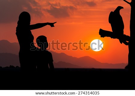 silhouette of mother and son point look at to eagle bird sitting on the timber sky on the sunset background