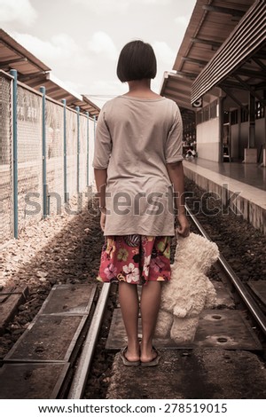 vintage tone, girl standing alone and hand hold white bear at Railway Platform