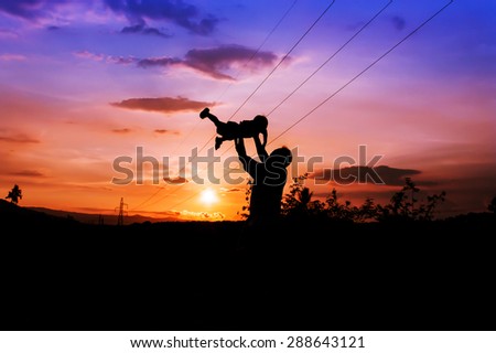 silhouettes of father and son play at mountain range and high voltage electricity pylon sunset background