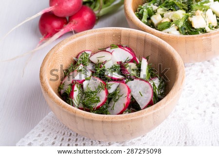 Mixed salad with red radish and dill in wooden bowl on white table.