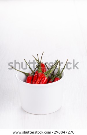 Red hot chili peppers in the cup on white wooden background. Cayenne pepper. Copy space.