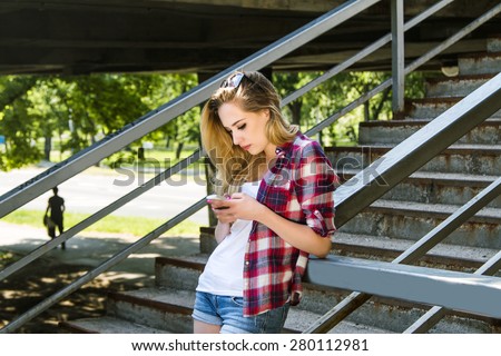Young beautiful hipster girl typing on smart phone on the street. Youth street style.