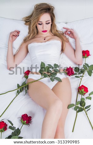 Sexy girl in white corset and panties underwear lying on the bed with roses, eyes closed, romance concept